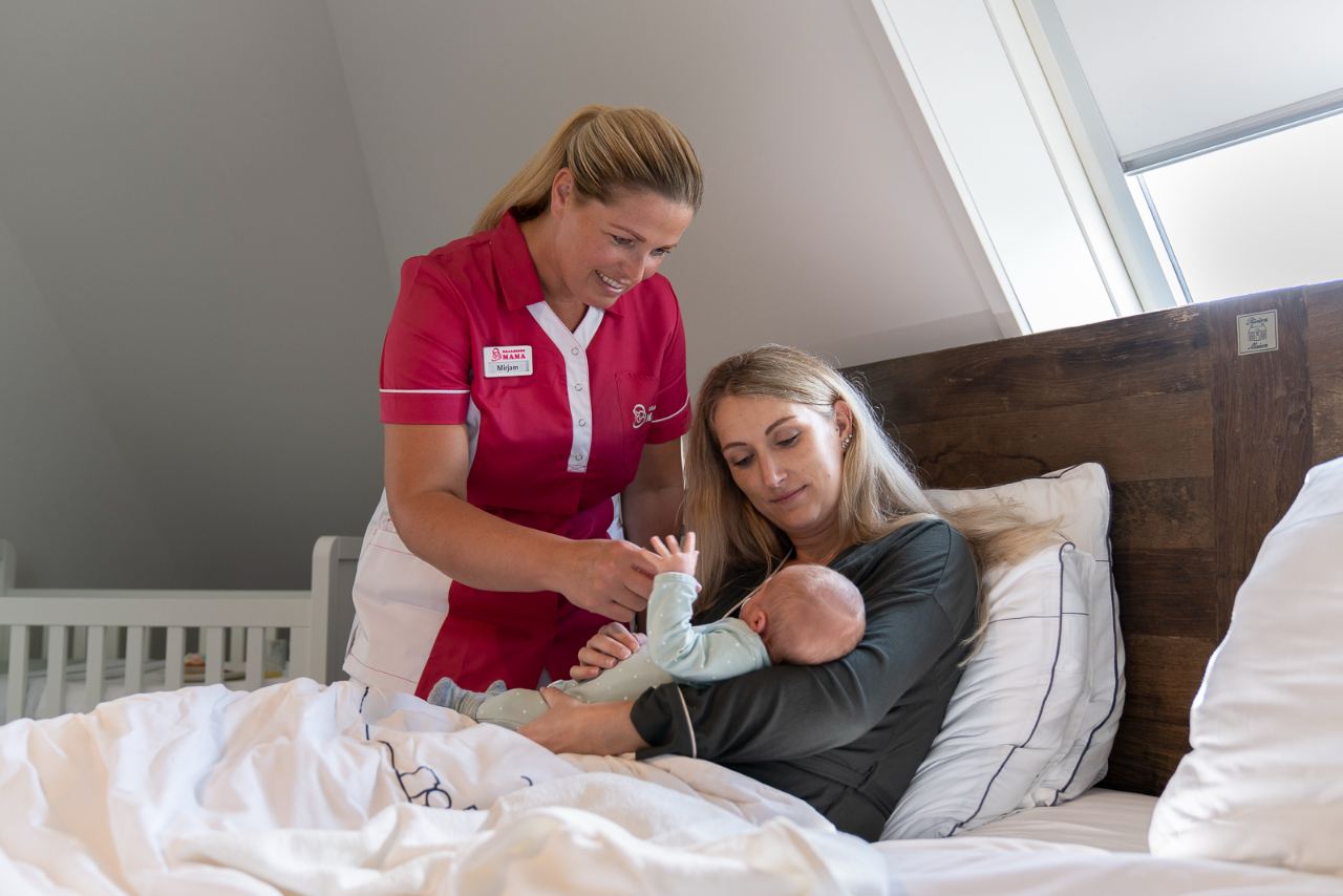 Kraamverzorgende helpt moeder en baby aan het bed tijdens de kraamweek