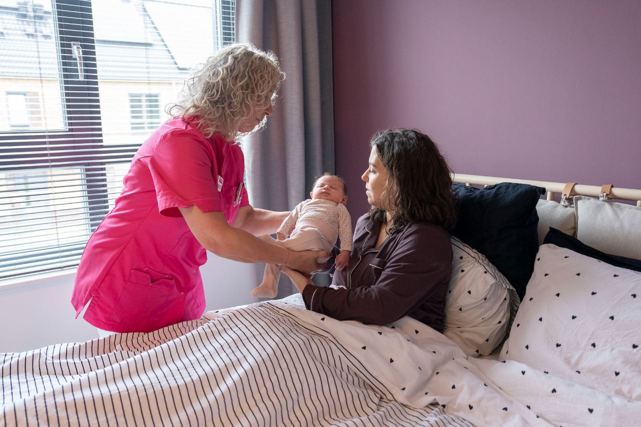 Kraamverzorgende van Kraamzorg Mama geeft moeder en baby aandacht aan het bed
